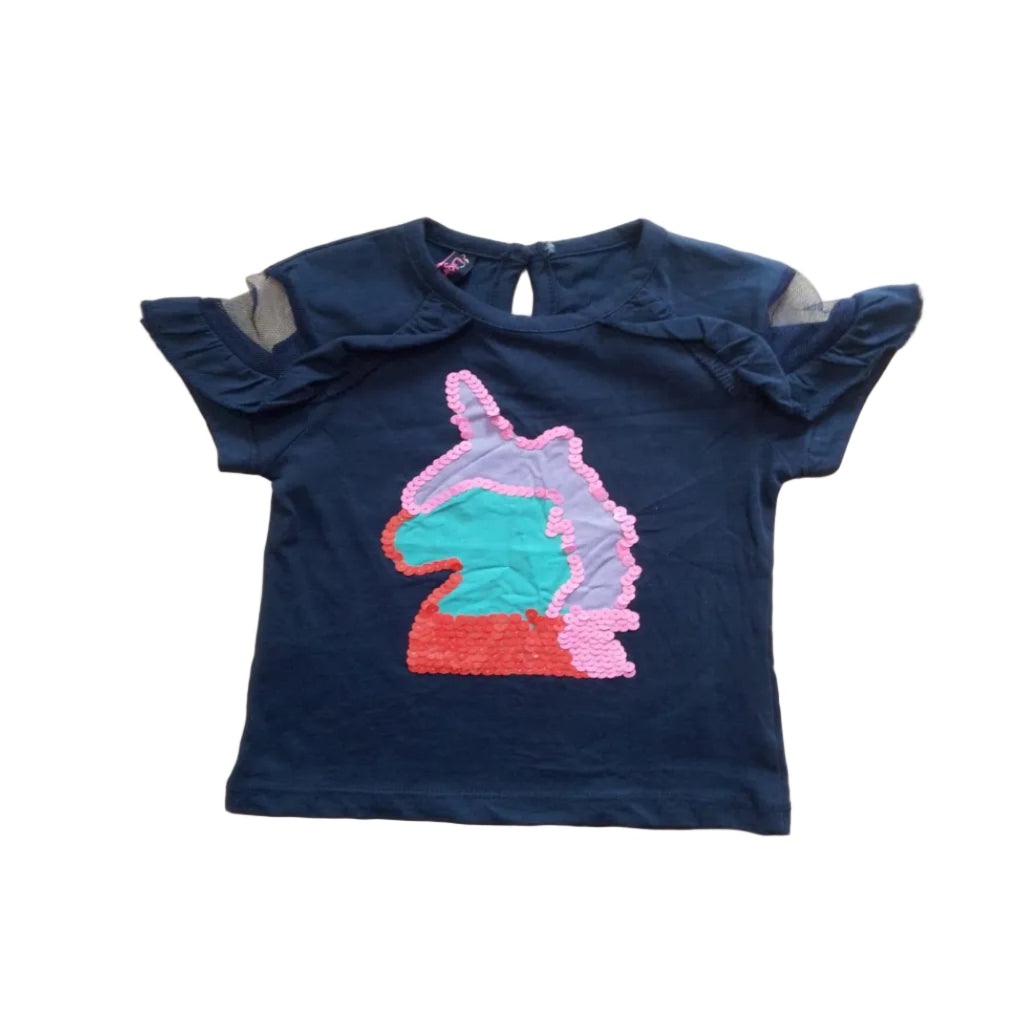 A navy blue short-sleeve children's top with ruffled shoulders and a sequined unicorn head patch on the front, laid flat on a light wood surface.