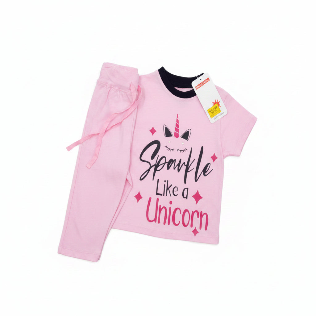 A pink children's two-piece outfit consisting of a short-sleeve top and matching pants, laid flat on a light wood surface. The top features a unicorn graphic with the text 'Unicorn Like a Spewf*ck' in stylized lettering.