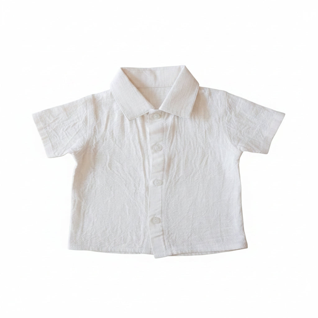 A white short-sleeve button-up shirt with a pointed collar, laid flat on a light wood surface. A red and yellow 'CHIKKUM MINDOS' brand hangtag is attached to the chest.